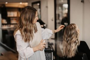 آرایشگر حرفه‌ای در حال اسپری زدن به موهای بلوند مشتری در سالن زیبایی - مدیریت زمان آرایشگاه در پیک کاری با qtik.app.